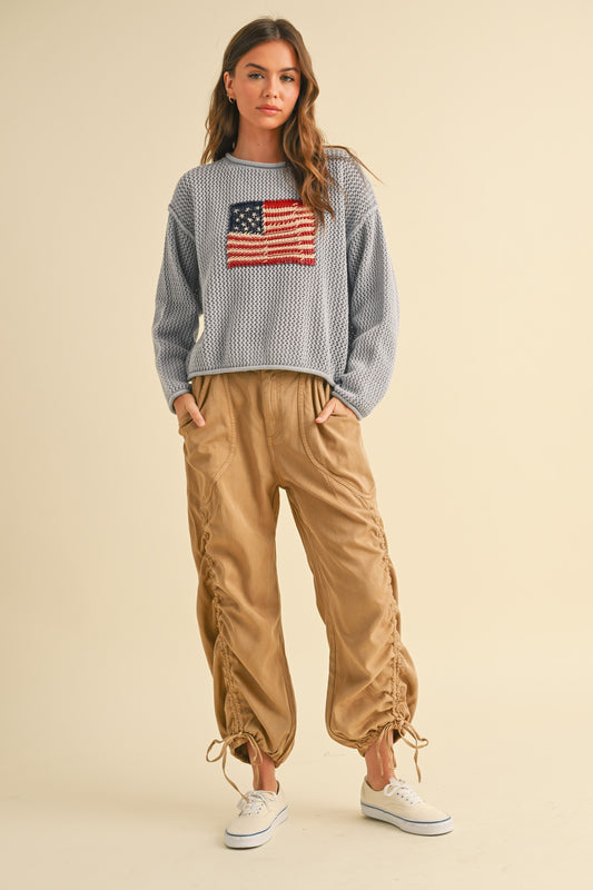 Woman wearing a sweater with an American flag design and beige pants on a beige background