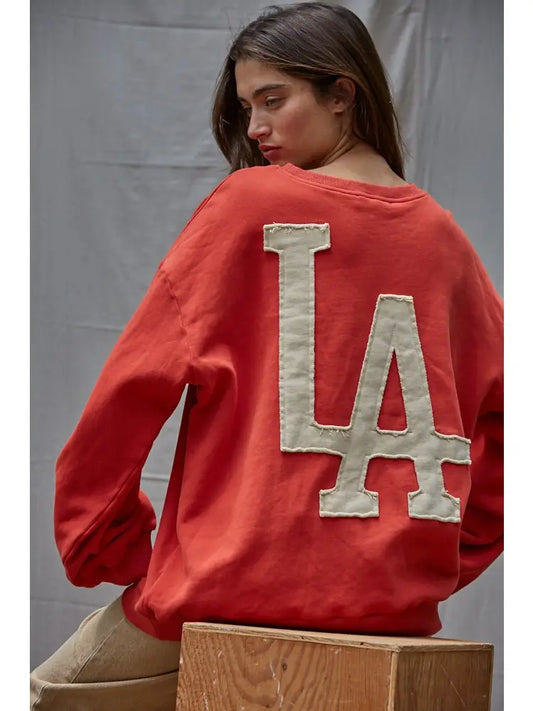 Person wearing a red sweatshirt with 'LA' on the back against a gray background